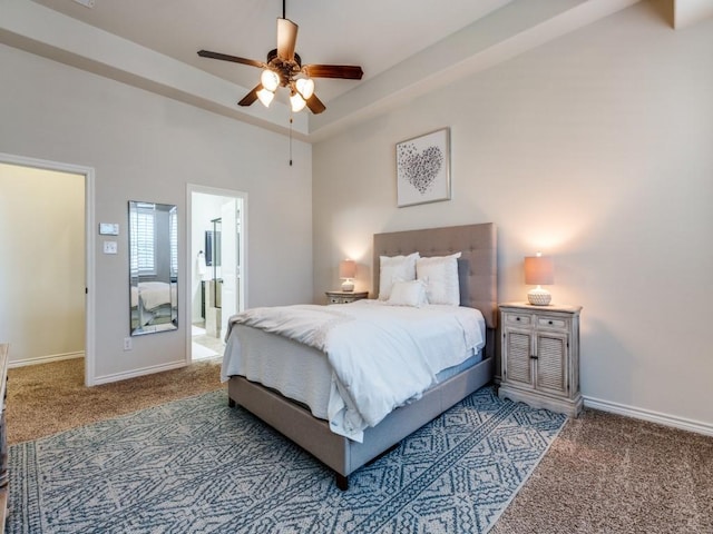 carpeted bedroom with connected bathroom, baseboards, a tray ceiling, and ceiling fan