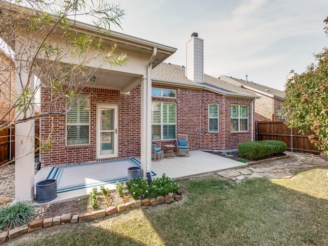 rear view of property with a patio, fence, a yard, a chimney, and brick siding