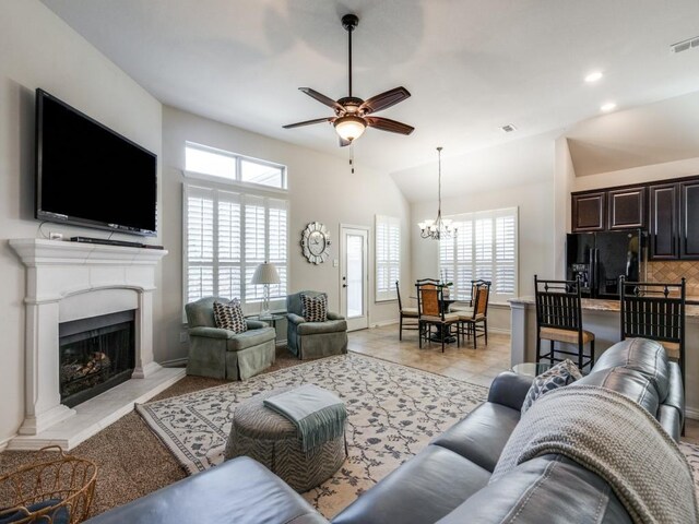 living area featuring a fireplace with raised hearth, baseboards, vaulted ceiling, recessed lighting, and ceiling fan with notable chandelier