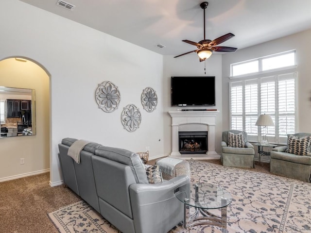 living area with visible vents, arched walkways, carpet, and a fireplace with raised hearth