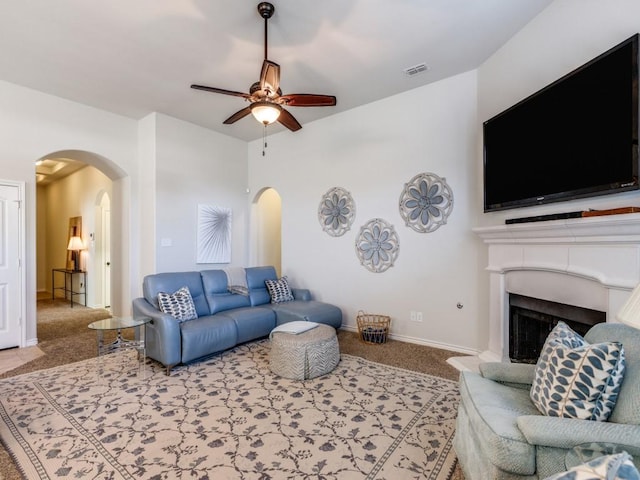 carpeted living area featuring visible vents, a fireplace with raised hearth, baseboards, ceiling fan, and arched walkways