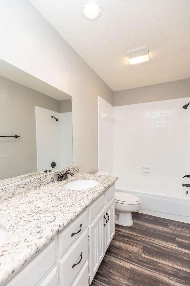 bathroom with toilet, vanity, shower / bathtub combination, wood finished floors, and a textured ceiling