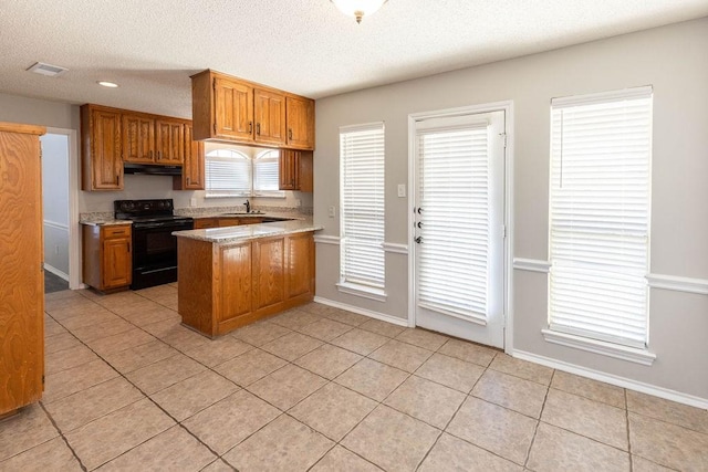 kitchen with brown cabinetry, visible vents, a peninsula, electric range, and under cabinet range hood