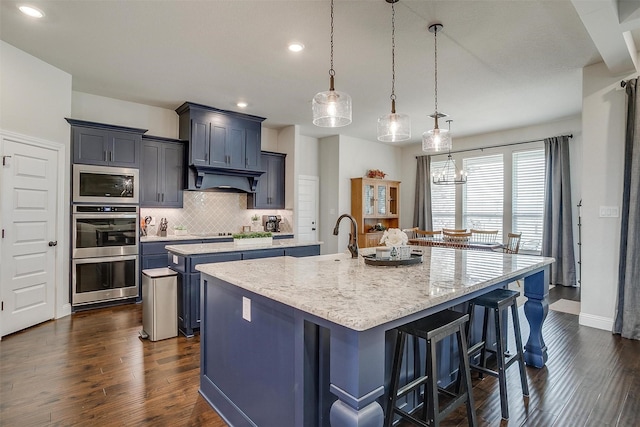 kitchen with a center island with sink, decorative backsplash, a kitchen breakfast bar, stainless steel appliances, and dark wood-style flooring