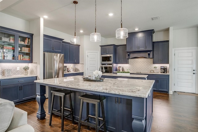 kitchen with visible vents, light stone countertops, appliances with stainless steel finishes, and a center island with sink