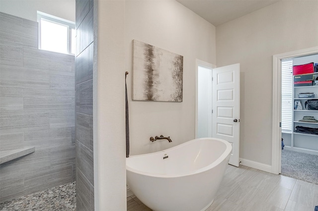 bathroom with tiled shower, baseboards, and a freestanding tub