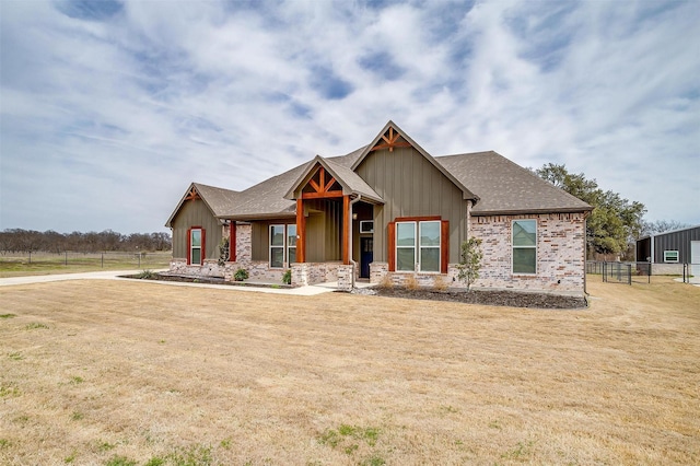 view of front facade with board and batten siding, a front yard, roof with shingles, and fence