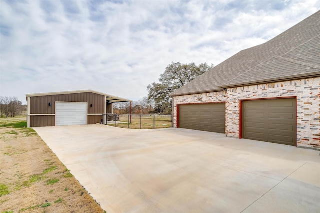 view of home's exterior featuring fence, a shingled roof, an outdoor structure, a detached garage, and board and batten siding