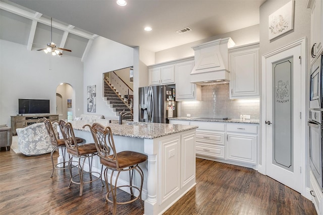 kitchen with visible vents, arched walkways, custom exhaust hood, stainless steel appliances, and dark wood-style flooring