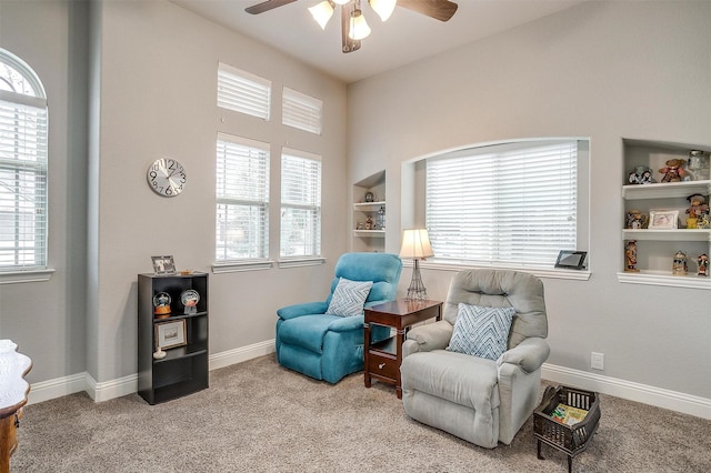 sitting room with built in features, baseboards, carpet, and a ceiling fan