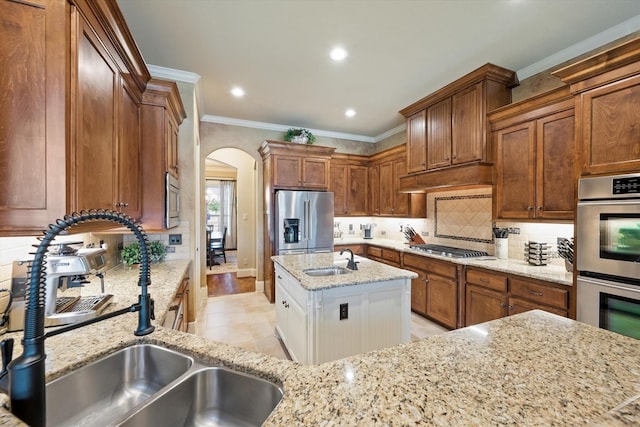 kitchen featuring light stone countertops, arched walkways, appliances with stainless steel finishes, and a sink