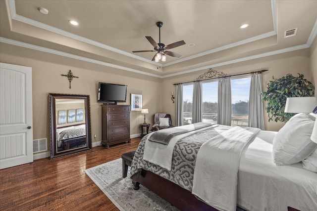 bedroom with a raised ceiling, dark wood-style floors, visible vents, and ornamental molding