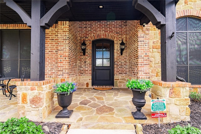 view of exterior entry with brick siding and covered porch