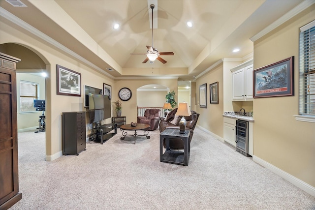 living room featuring a ceiling fan, beverage cooler, arched walkways, light colored carpet, and indoor bar