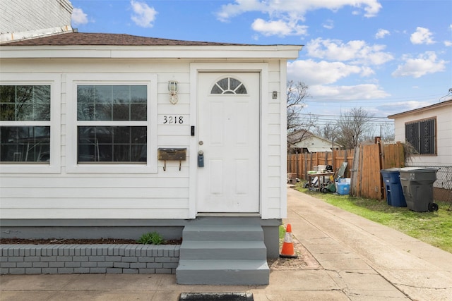 property entrance featuring a shingled roof and fence