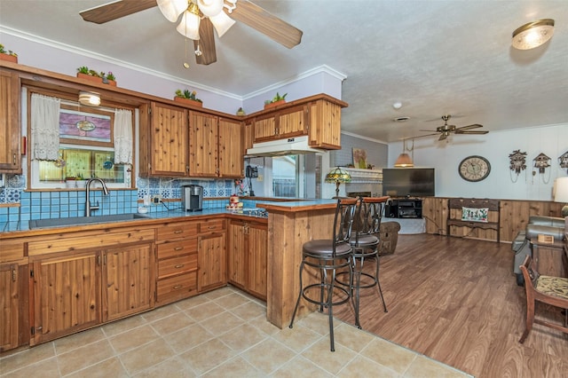 kitchen featuring crown molding, open floor plan, decorative backsplash, brown cabinetry, and a sink