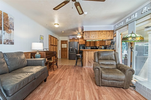 living area featuring light wood-style floors, ornamental molding, and a ceiling fan