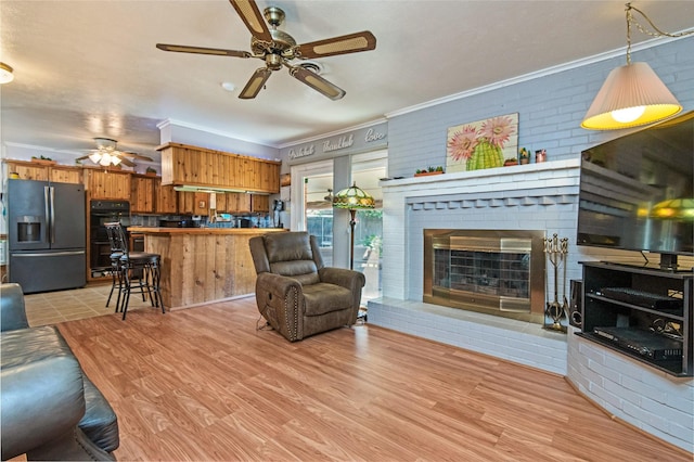 living room with crown molding, light wood-style flooring, and a brick fireplace