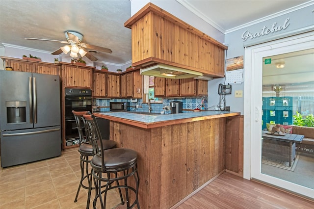 kitchen featuring tasteful backsplash, ornamental molding, a peninsula, brown cabinetry, and black appliances