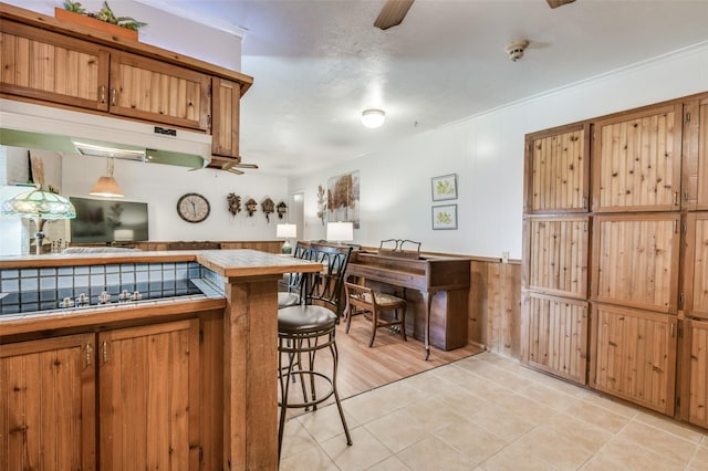 kitchen featuring brown cabinets, a kitchen bar, ceiling fan, and tile counters