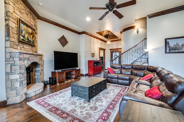 living area featuring stairway, a ceiling fan, wood finished floors, ornamental molding, and a stone fireplace