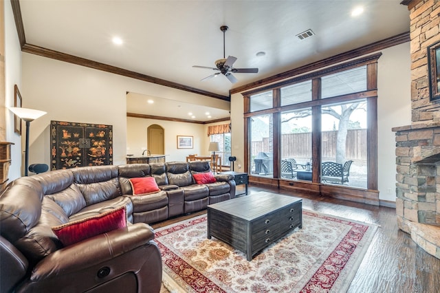 living room with wood finished floors, visible vents, arched walkways, ornamental molding, and a stone fireplace