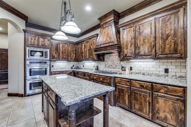 kitchen featuring light stone countertops, premium range hood, ornamental molding, decorative backsplash, and appliances with stainless steel finishes