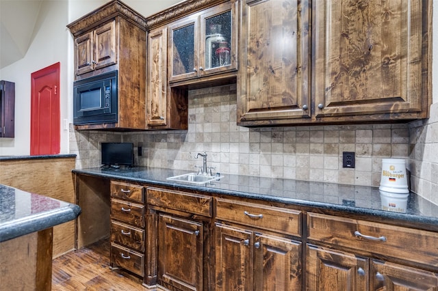 kitchen featuring tasteful backsplash, wood finished floors, black microwave, and a sink