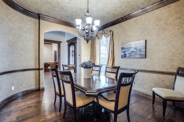 dining room featuring wood finished floors, arched walkways, crown molding, a notable chandelier, and a textured wall