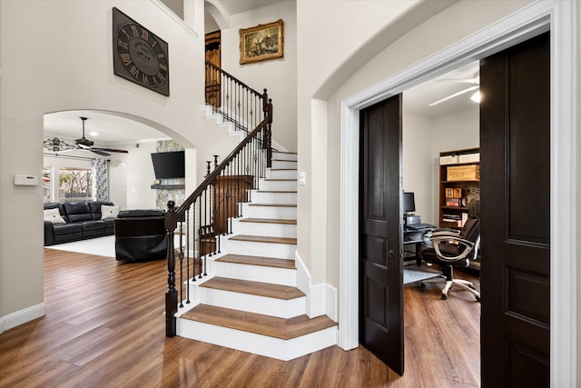 staircase with baseboards, wood finished floors, arched walkways, and ceiling fan