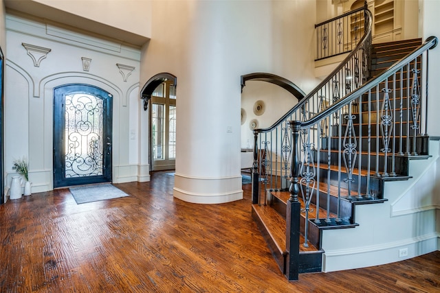 foyer entrance with stairs, wood finished floors, arched walkways, and a towering ceiling