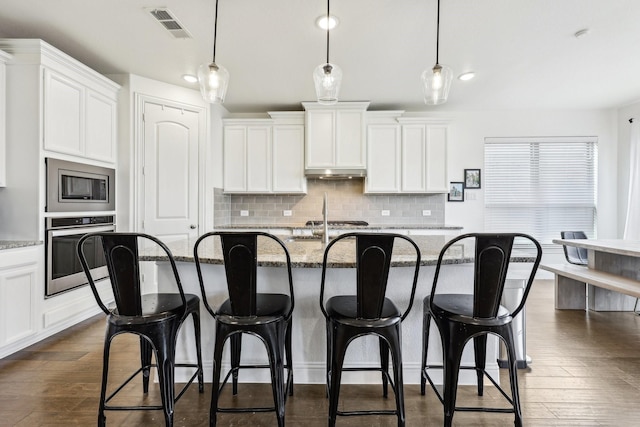 kitchen with a kitchen breakfast bar, visible vents, dark wood-style flooring, and stainless steel appliances