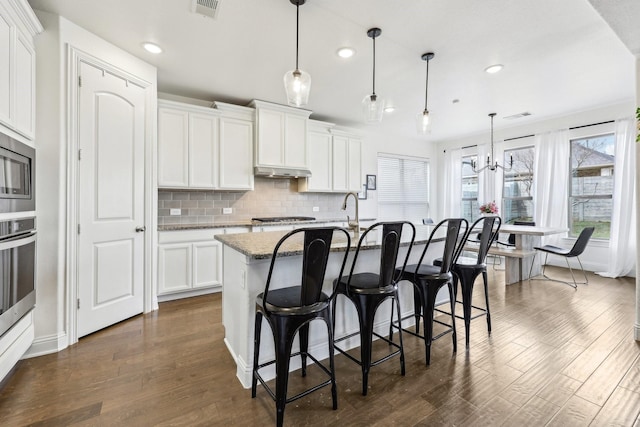 kitchen with visible vents, under cabinet range hood, dark wood finished floors, a breakfast bar area, and decorative backsplash