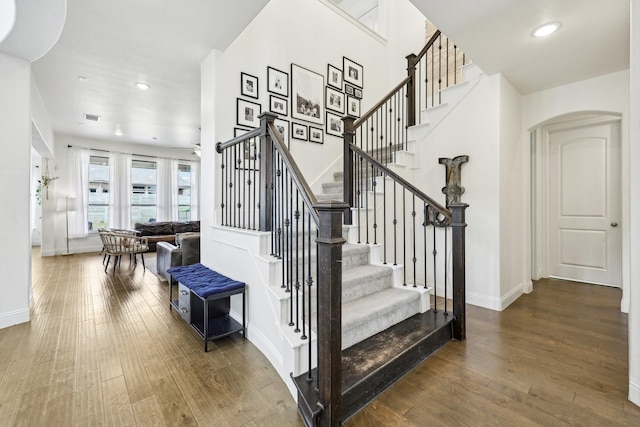 stairway featuring recessed lighting, visible vents, arched walkways, and wood-type flooring