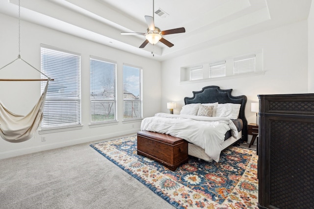 bedroom featuring a ceiling fan, baseboards, visible vents, a tray ceiling, and carpet flooring