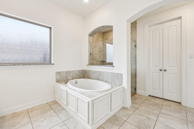 bathroom featuring tile patterned flooring, tiled shower, a bath, and baseboards