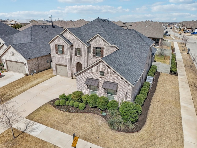 view of front of house with brick siding, an attached garage, a residential view, roof with shingles, and driveway