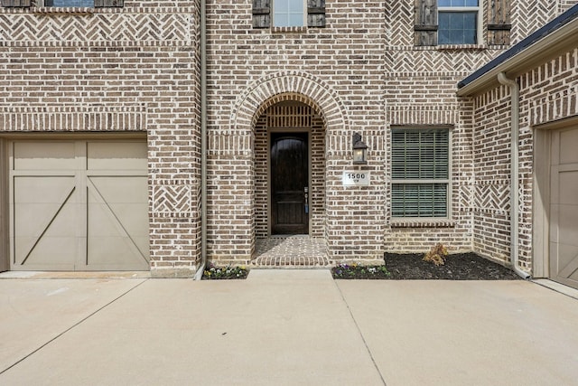 doorway to property with brick siding, driveway, and a garage