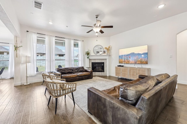 living room featuring visible vents, dark wood-type flooring, a ceiling fan, a tiled fireplace, and arched walkways