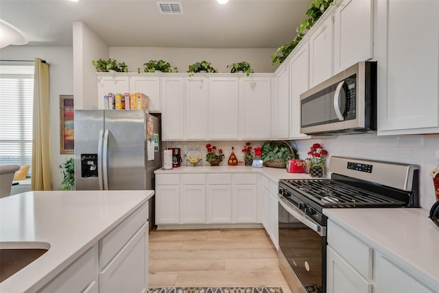 kitchen featuring visible vents, white cabinetry, stainless steel appliances, light countertops, and decorative backsplash