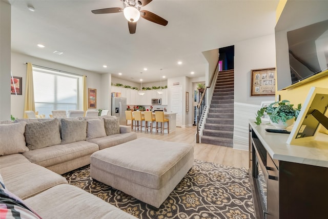 living room featuring a wainscoted wall, stairs, recessed lighting, light wood-style flooring, and a ceiling fan