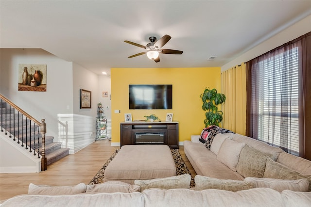 living room featuring a ceiling fan, a glass covered fireplace, wood finished floors, baseboards, and stairs