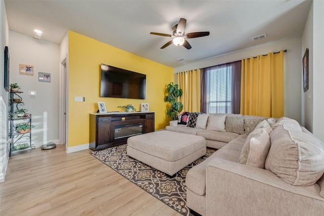 living room featuring visible vents, baseboards, wood finished floors, and a ceiling fan