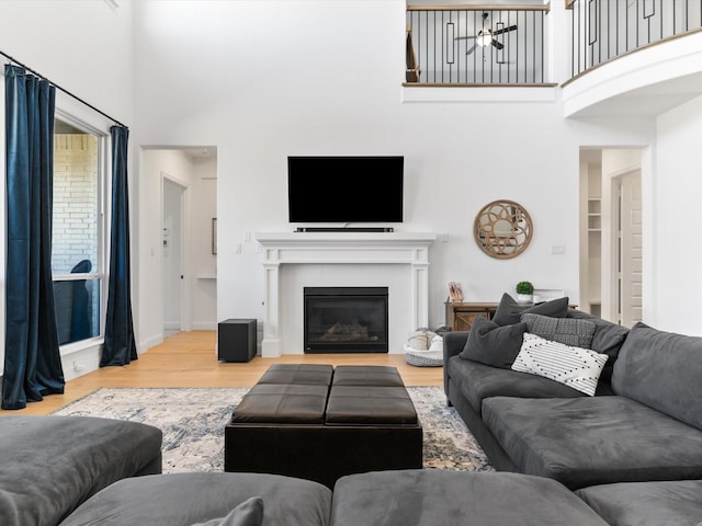 living room featuring wood finished floors, a glass covered fireplace, a high ceiling, baseboards, and ceiling fan