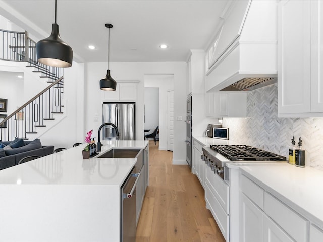 kitchen with premium range hood, light wood-style flooring, a sink, appliances with stainless steel finishes, and tasteful backsplash