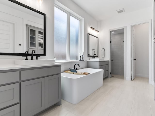 bathroom featuring a stall shower, visible vents, a freestanding tub, and a sink