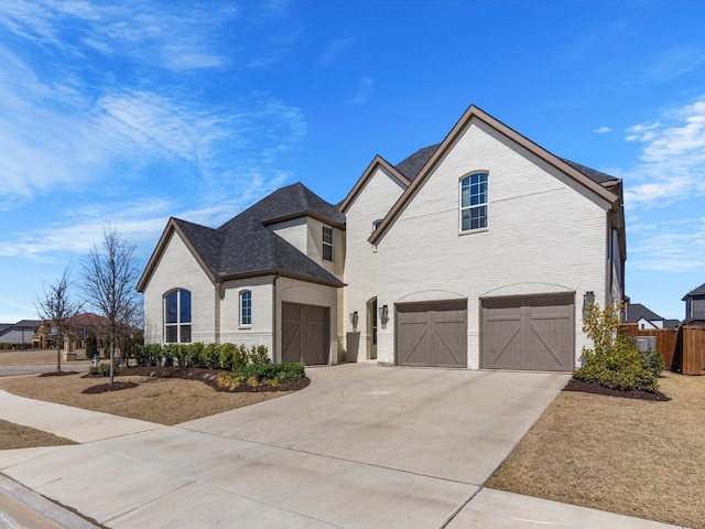 french country home with brick siding, concrete driveway, and an attached garage