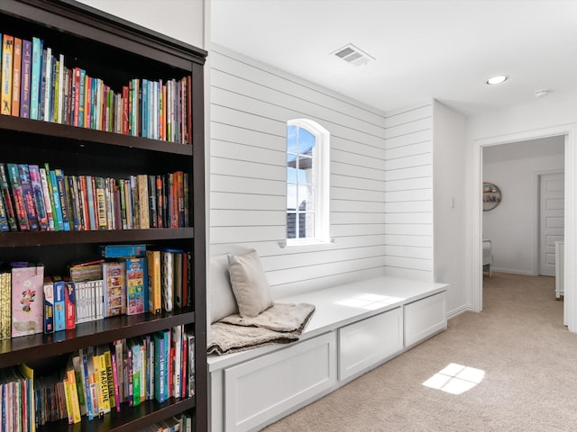 living area with wooden walls, visible vents, and light carpet