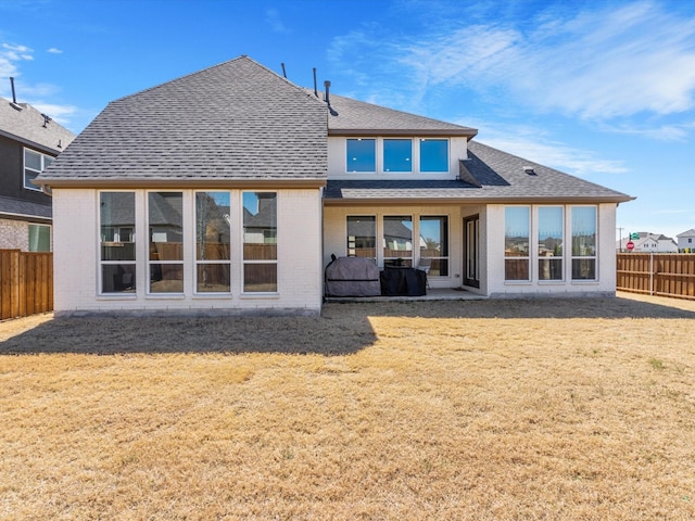 back of house with brick siding, roof with shingles, a yard, a fenced backyard, and a patio area