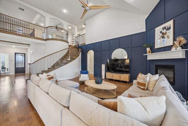 living room with stairway, visible vents, arched walkways, wood-type flooring, and a glass covered fireplace